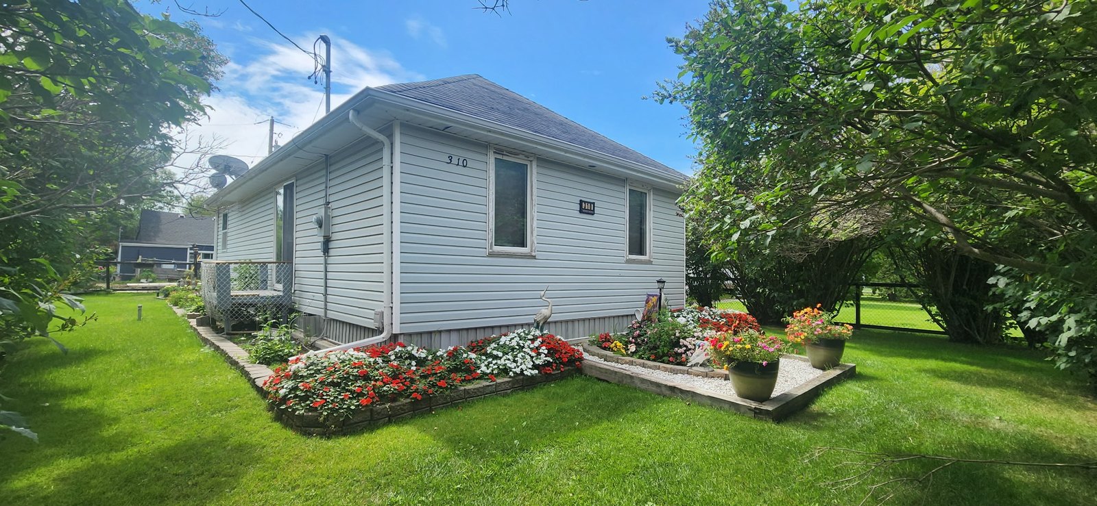 310 Epsilon Avenue, Winnipeg Beach &middot; 310 Epsilon Avenue from the front corner, with planted flower beds edging the lawn