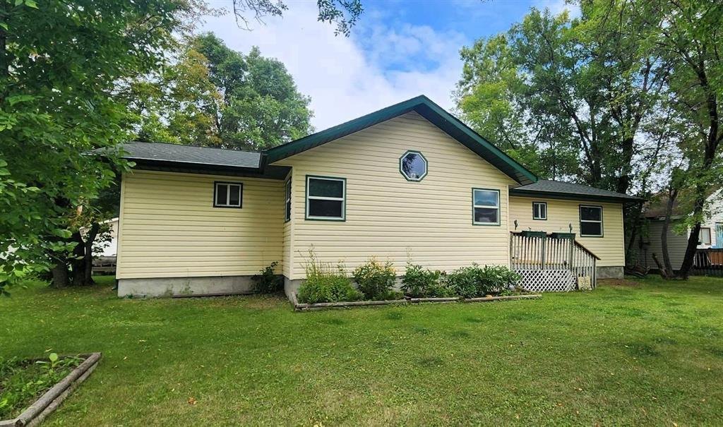 325 Epsilon Avenue, Winnipeg Beach &middot; the front of the bungalow with its yellow siding and green trim, set among mature trees
